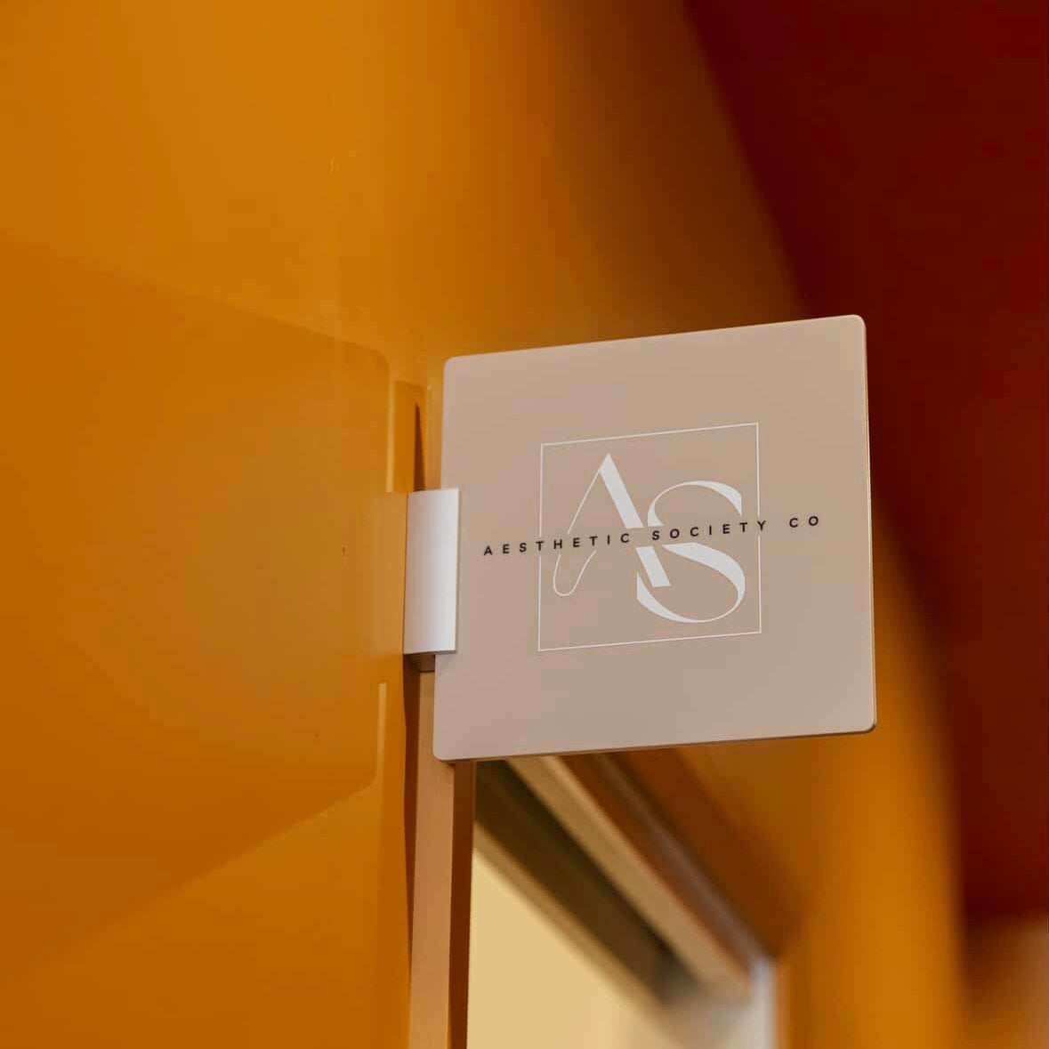 Custom acrylic square blade sign with logo for Aesthetic Society Co mounted on wall for business branding