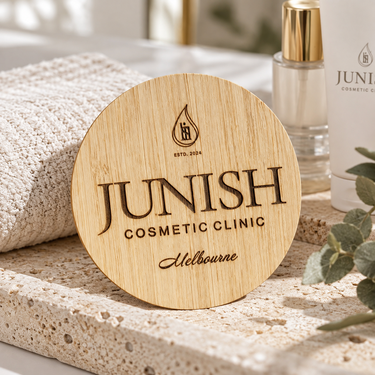 Engraved bamboo branding disc for Junish Cosmetic Clinic, styled with skincare products and natural spa décor for branded product photography.