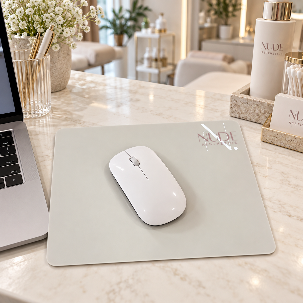 Custom nude acrylic mouse pad with Nude Aesthetics branding and white wireless mouse, displayed on a modern beauty clinic reception desk.