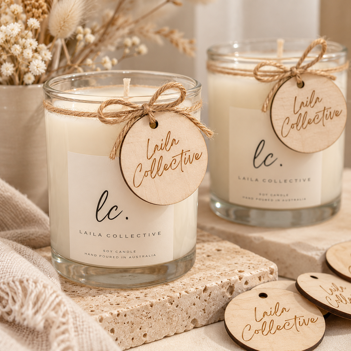 Custom round wooden tags engraved with Laila Collective branding, tied with natural twine to glass soy candles in a neutral setting with dried flowers.