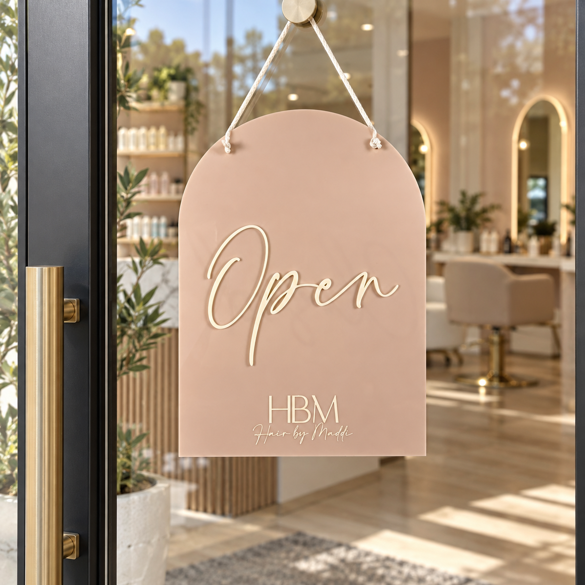 Custom blush acrylic open sign with raised cream lettering and HBM Hair by Maddi branding, hanging on a modern glass salon door.