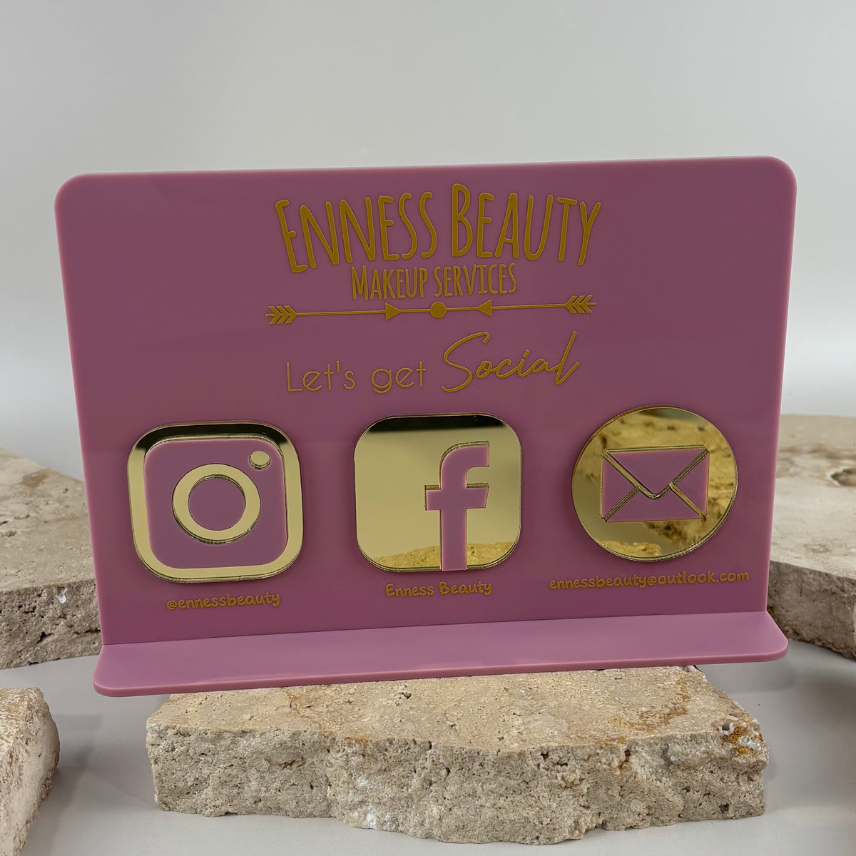 Custom pink acrylic countertop social media sign for Enness Beauty makeup services, featuring gold mirror Instagram, Facebook and email icons.