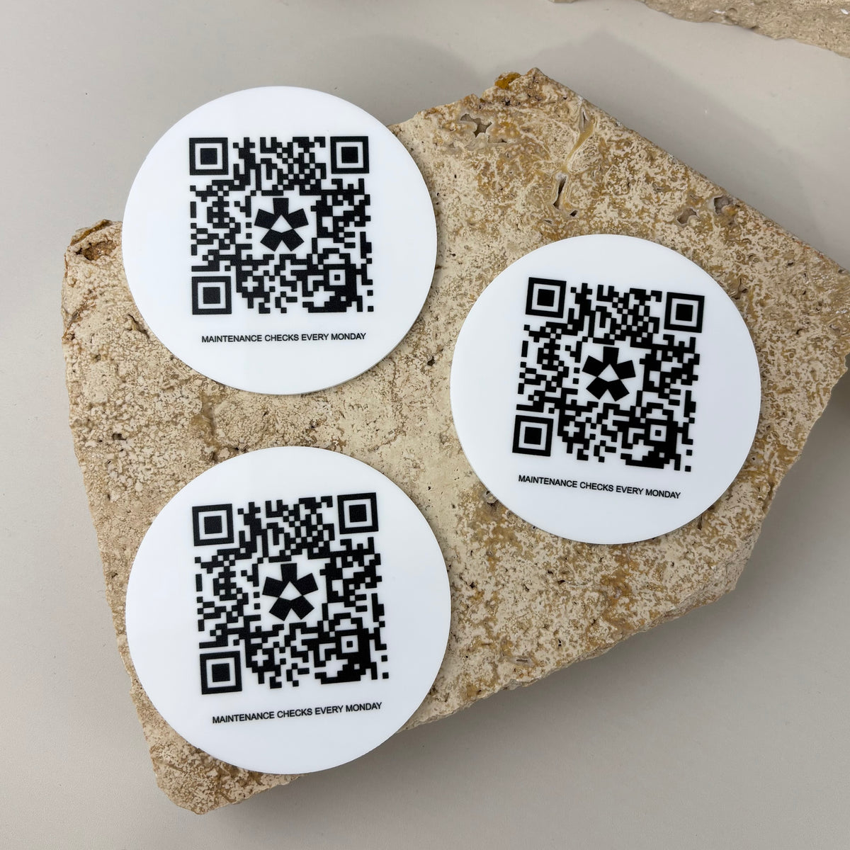 Three custom round white acrylic QR code discs with black printed scannable codes for weekly business maintenance checks and tracking.