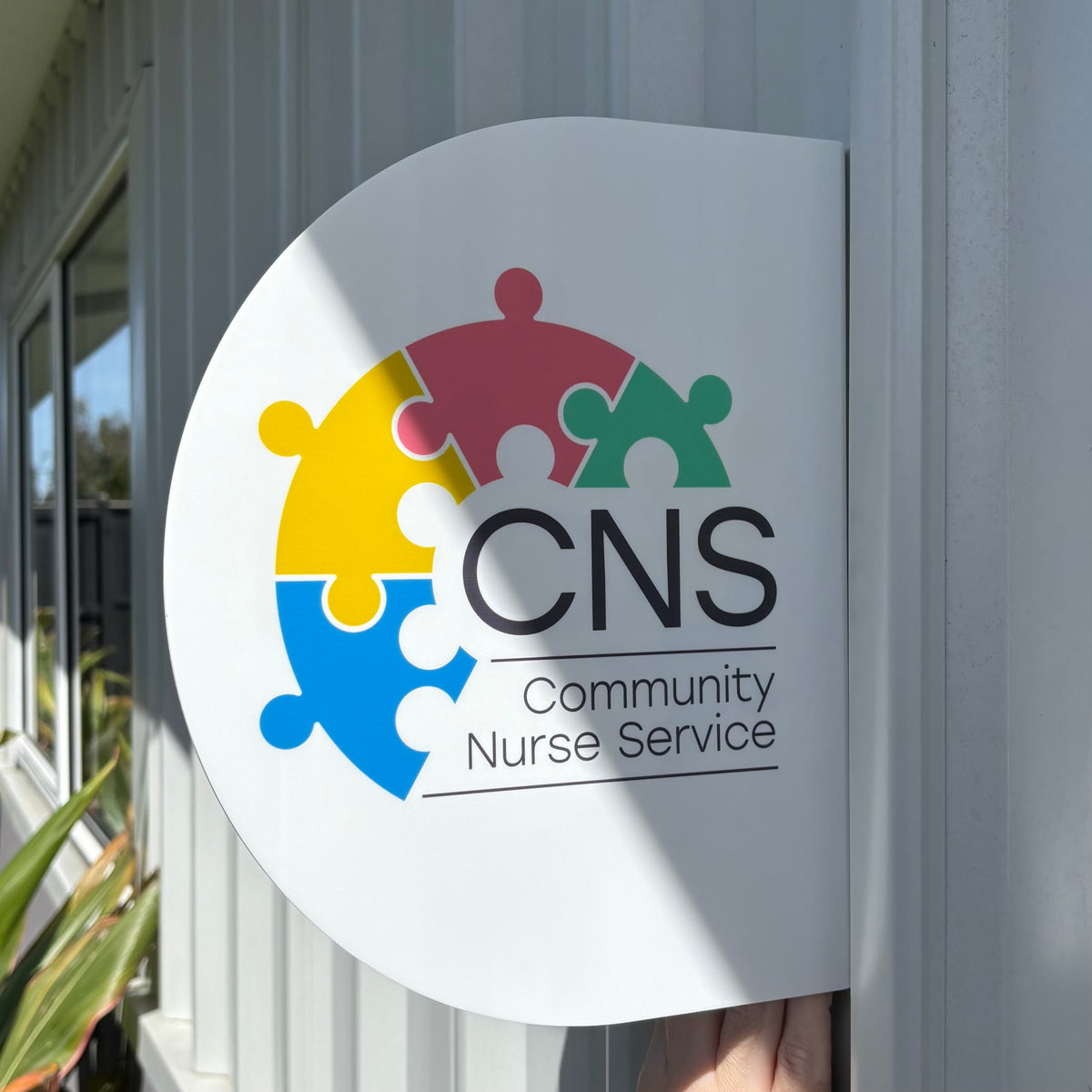 Custom round acrylic blade sign featuring the colourful CNS Community Nurse Service logo on a white background, designed for business entrance signage.