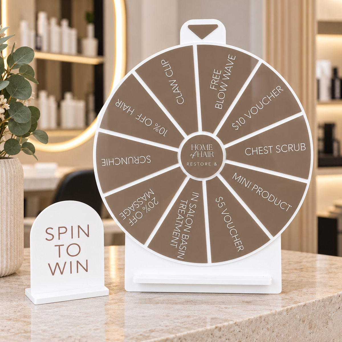 Custom taupe and white acrylic Spin to Win prize wheel featuring hair salon discounts, treatments and giveaways, displayed on a modern salon reception counter with a matching sign.