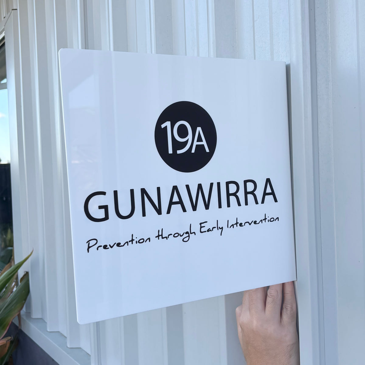 Custom square white acrylic business sign featuring black Gunawirra branding, 19A address and printed logo, displayed against an exterior wall.