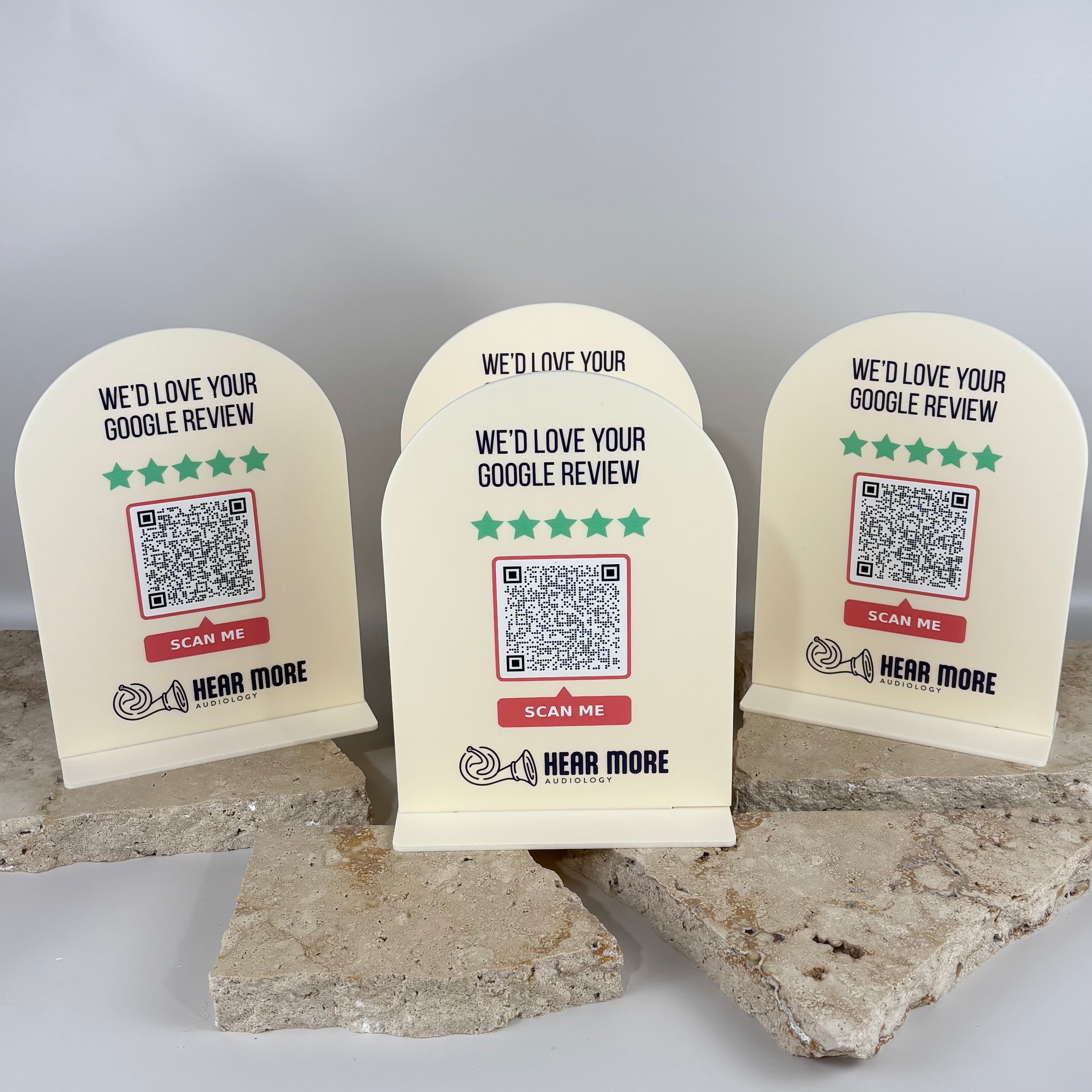 Custom acrylic Google review QR code counter signs for Hear More Audiology, featuring branded logo, five star rating graphics and scan me QR codes, designed for reception desks to encourage customer Google reviews in clinics and small businesses.