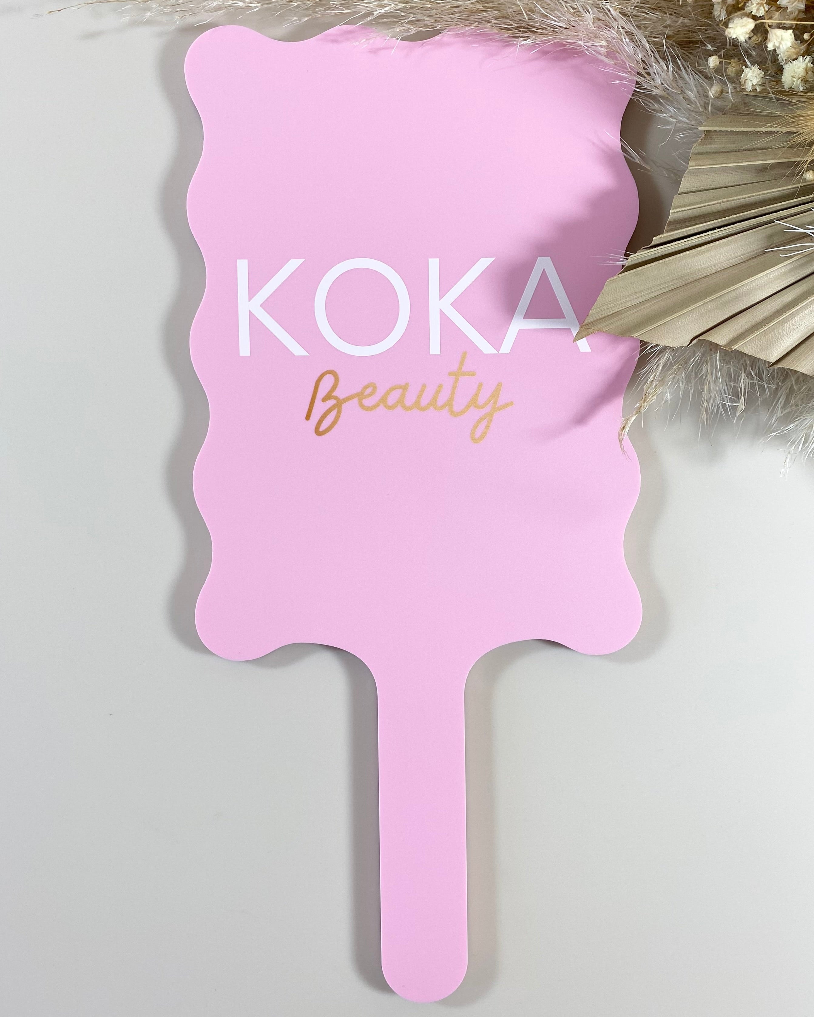 Pink wavy handheld mirror with Koka Beauty logo for salons