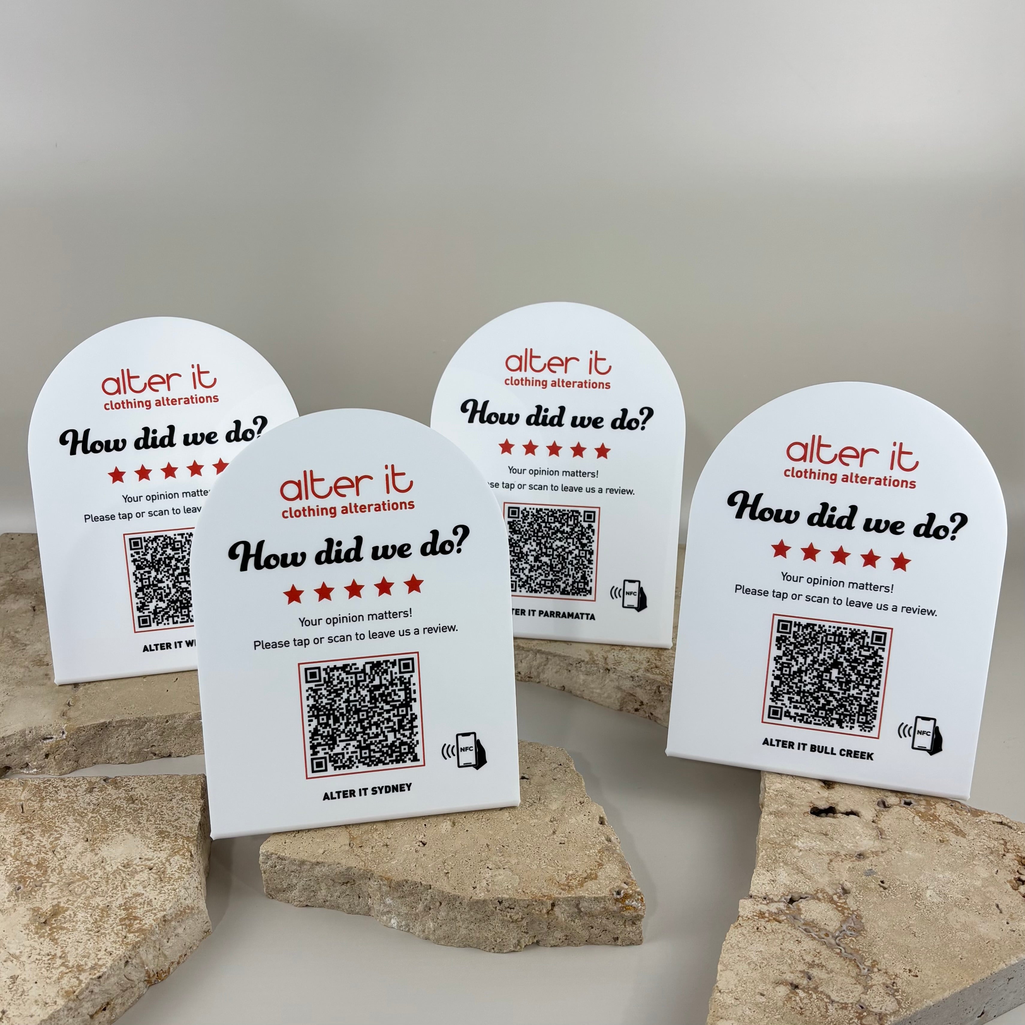 Custom white acrylic NFC Google review stands with QR codes for Alter It Clothing Alterations, featuring UV printed branding and contactless tap technology to encourage customer reviews across multiple store locations.
