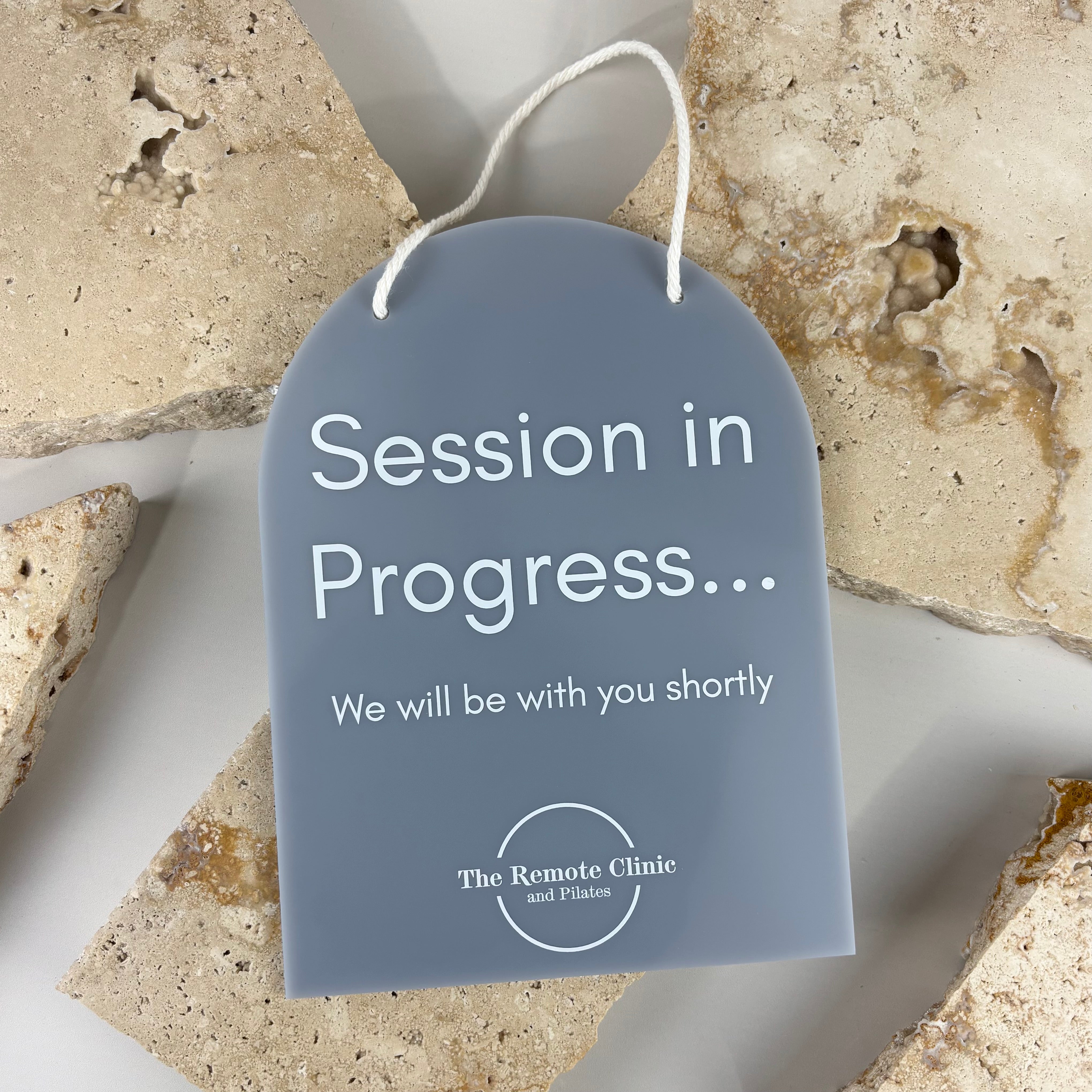 Frosted acrylic “Session in Progress” hanging door sign with rope hanger and engraved white text, professional clinic door sign designed for treatment rooms, physiotherapy clinics, beauty salons and wellness studios.