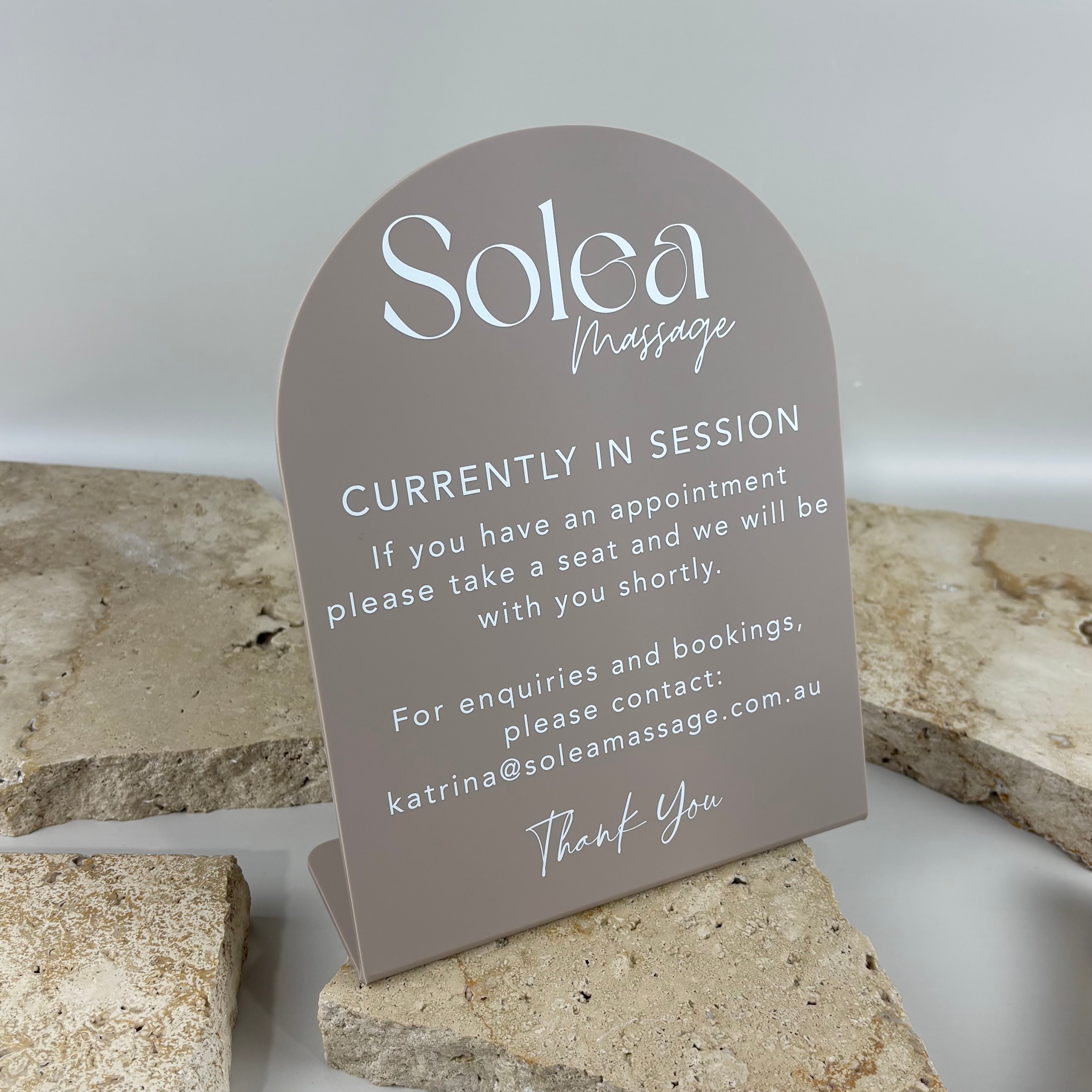 Minimalist arched acrylic counter sign for Solea Massage featuring white UV printed text on a taupe acrylic finish, displaying a currently in session message for a professional massage and wellness clinic.