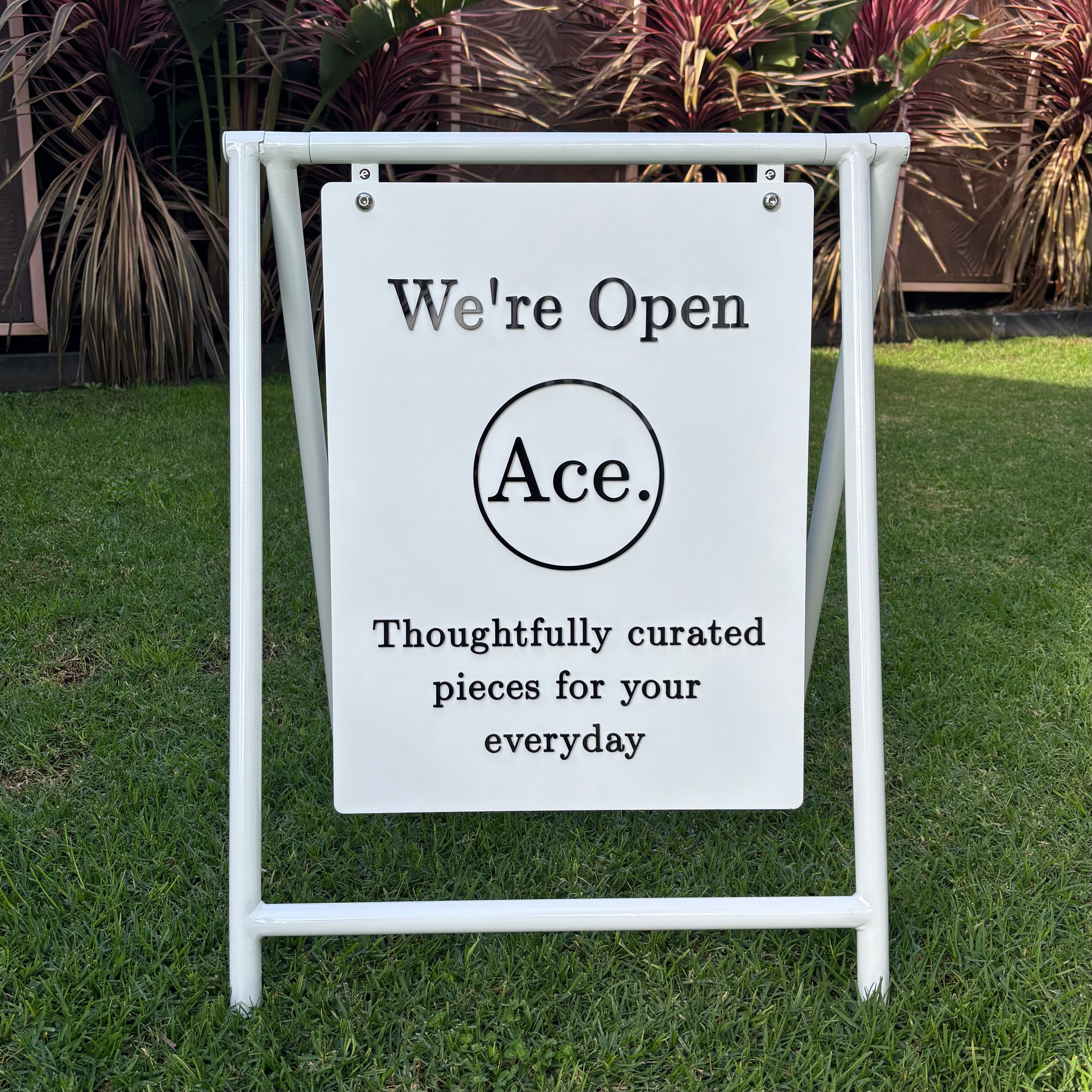 Custom white swing pavement sign with hanging acrylic panel, featuring black 3D lettering, business logo and “We’re Open” branding for a retail store.