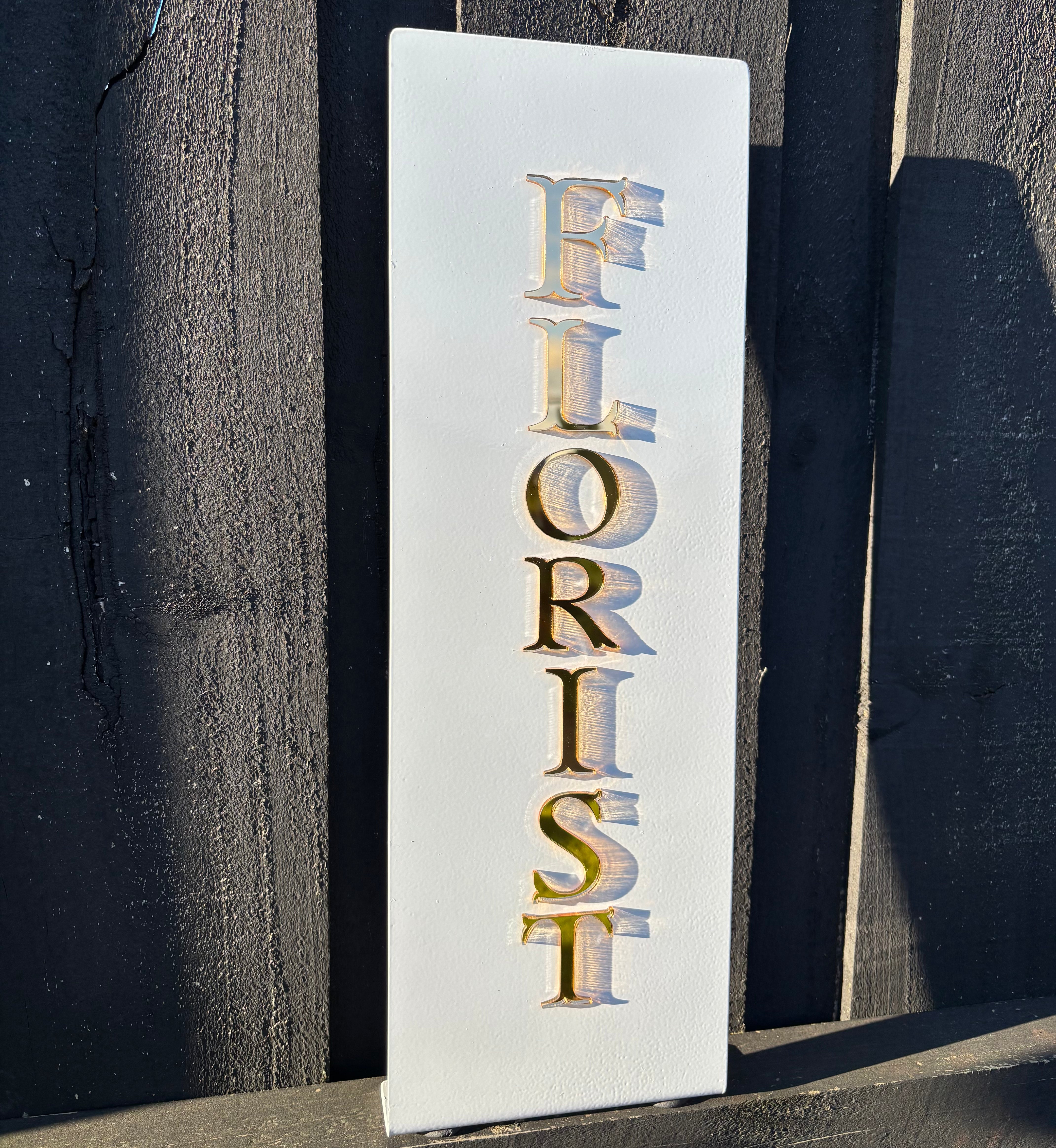Custom rectangle blade sign mounted vertically with gold lettering spelling ‘FLORIST’, outdoor business signage.