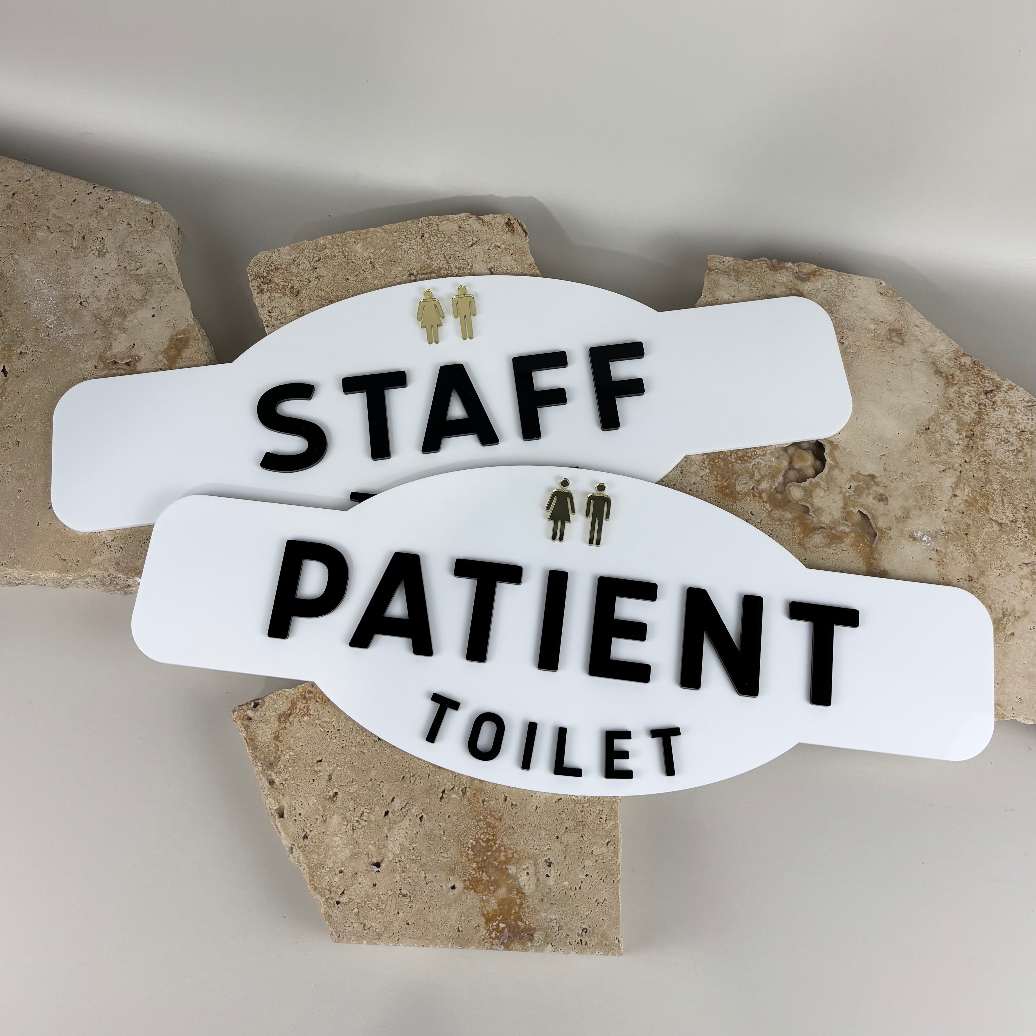 Custom acrylic toilet signs for staff and patients in white with black raised lettering and gold male and female icons, modern bathroom signage by Laser Edge Designs.