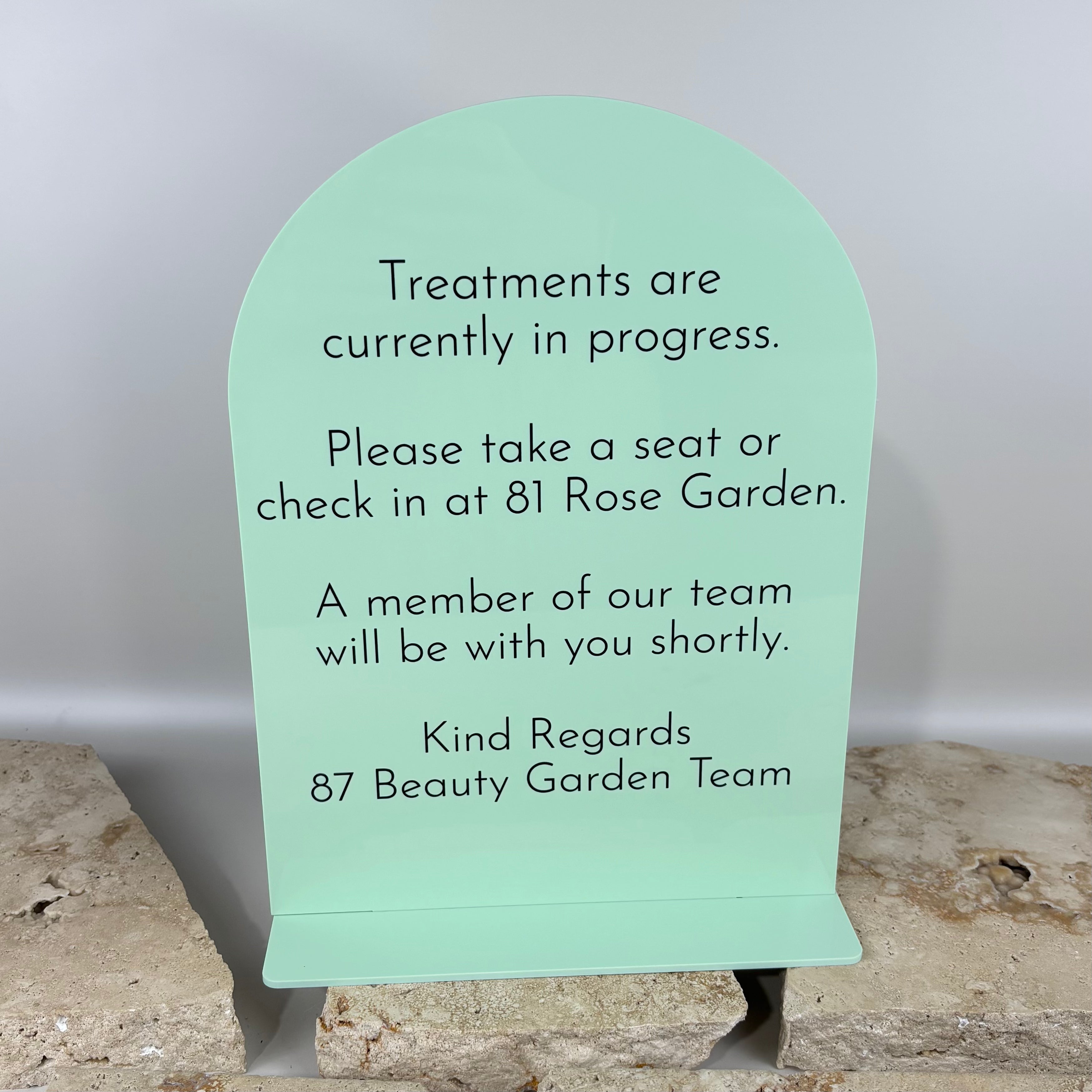 Mint green acrylic reception sign with arched top and black text, stating treatments are in progress, freestanding counter sign for beauty salon or clinic waiting area, professional custom acrylic signage for Australian businesses.