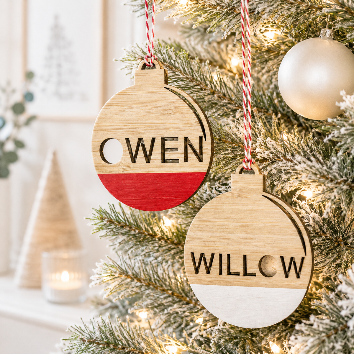 Personalised wooden Christmas baubles with custom cutout names, red and white painted details and festive twine, hanging on a modern Christmas tree.