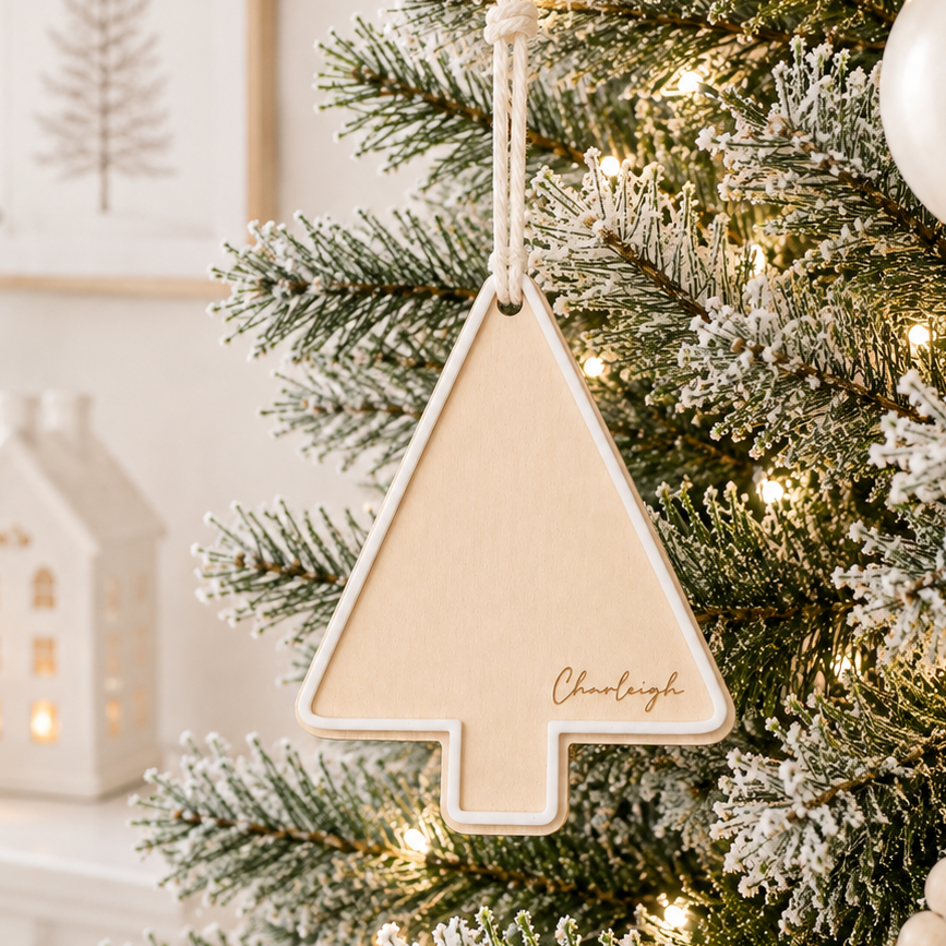 Personalised wooden Christmas tree bauble with custom engraved name and raised white acrylic border, hanging on a modern frosted Christmas tree.