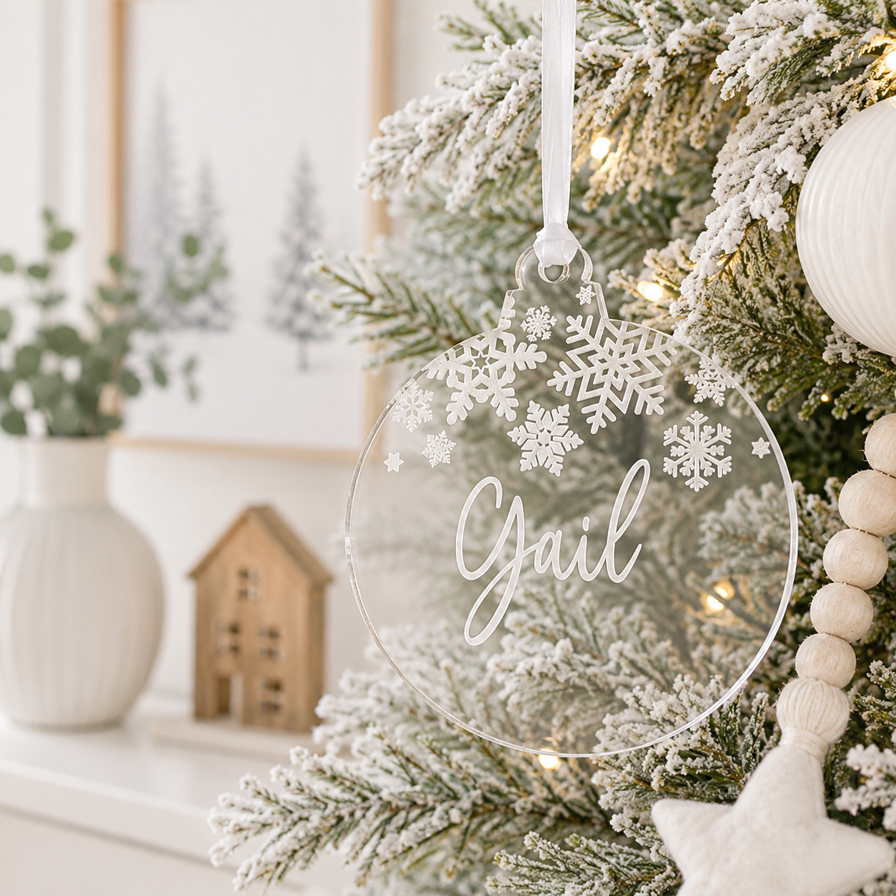 Personalised clear acrylic Christmas bauble with custom name and engraved snowflake design, hanging on a modern frosted Christmas tree.
