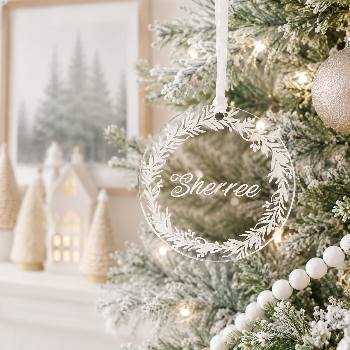 Personalised clear acrylic Christmas bauble with custom name and elegant botanical wreath design, hanging on a modern frosted Christmas tree.