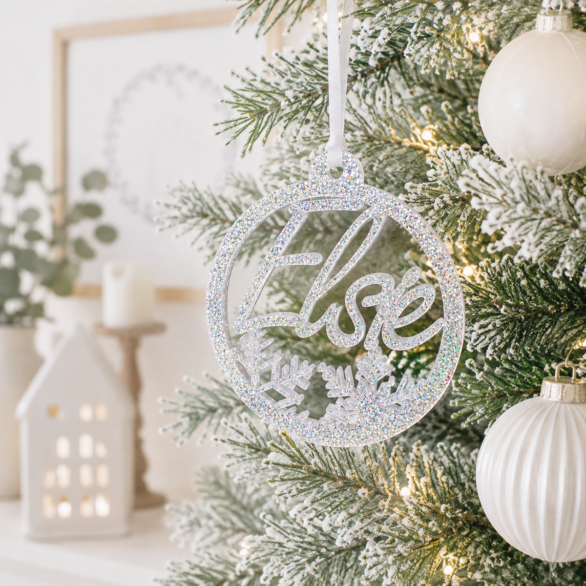 Personalised silver glitter acrylic Christmas bauble with custom name and snowflake design, hanging on a modern frosted Christmas tree.