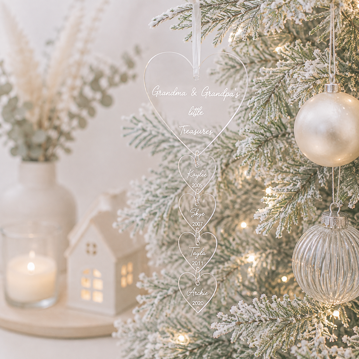 Personalised clear acrylic grandparents Christmas bauble with custom hanging hearts, grandchildren’s names and birth years, displayed on a modern Christmas tree.