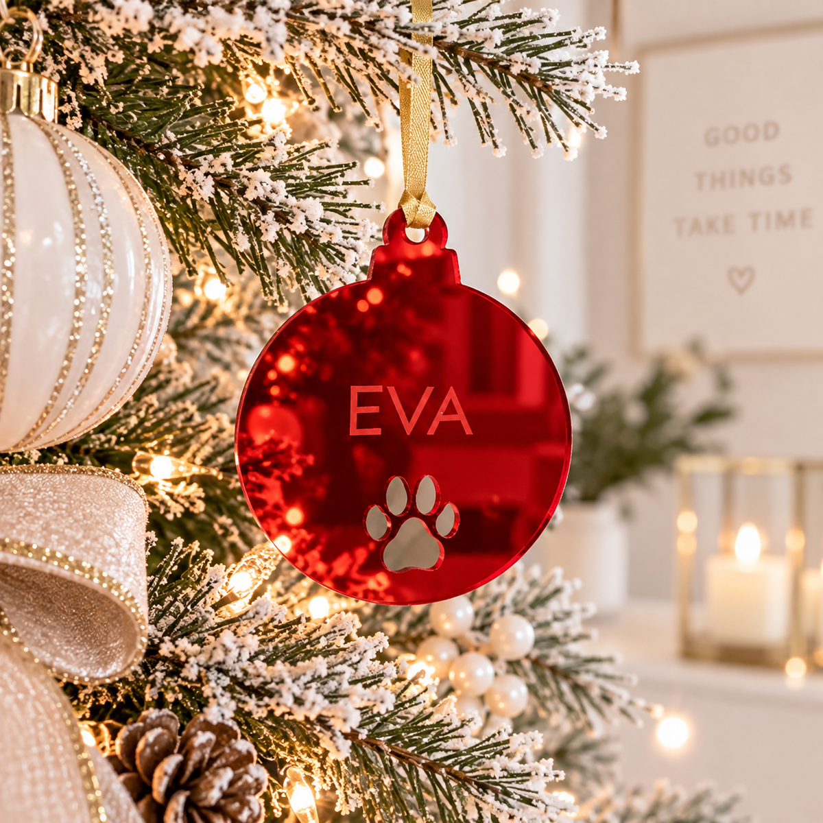 Personalised red mirror acrylic pet Christmas bauble with the name Eva and paw print, hanging on a light modern Christmas tree with festive decorations.