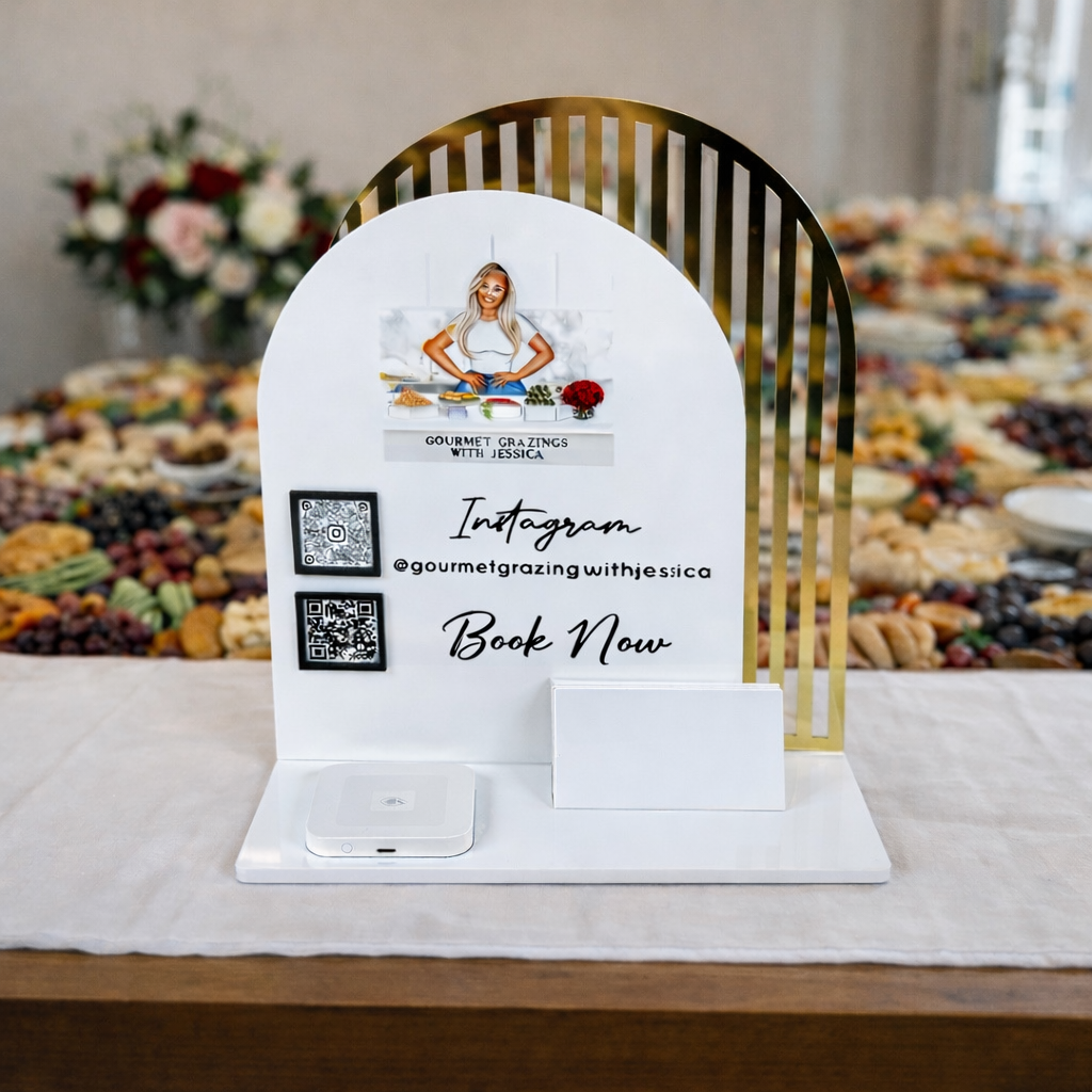 Custom acrylic NFC business stand for grazing business displayed on a table, featuring Gourmet Grazing with Jessica branding, Instagram QR code, book now text and wireless phone charging base