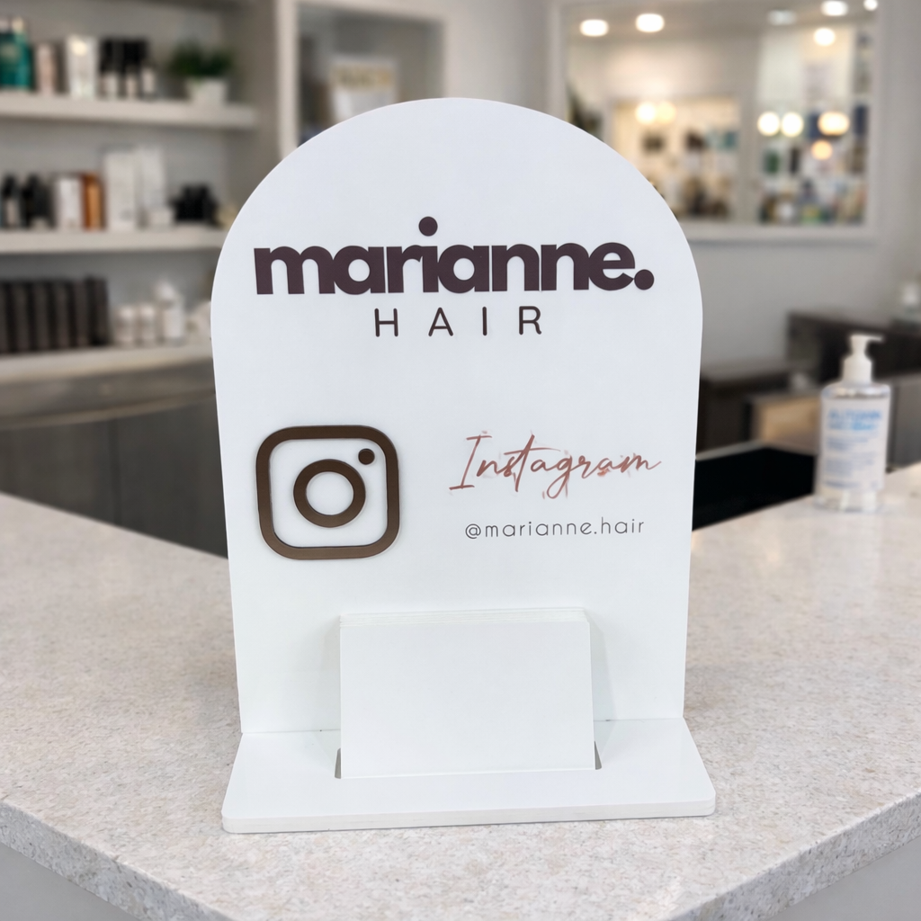 Custom white acrylic hair salon reception sign displayed on a hairdressing counter, featuring Marianne Hair branding and Instagram handle signage