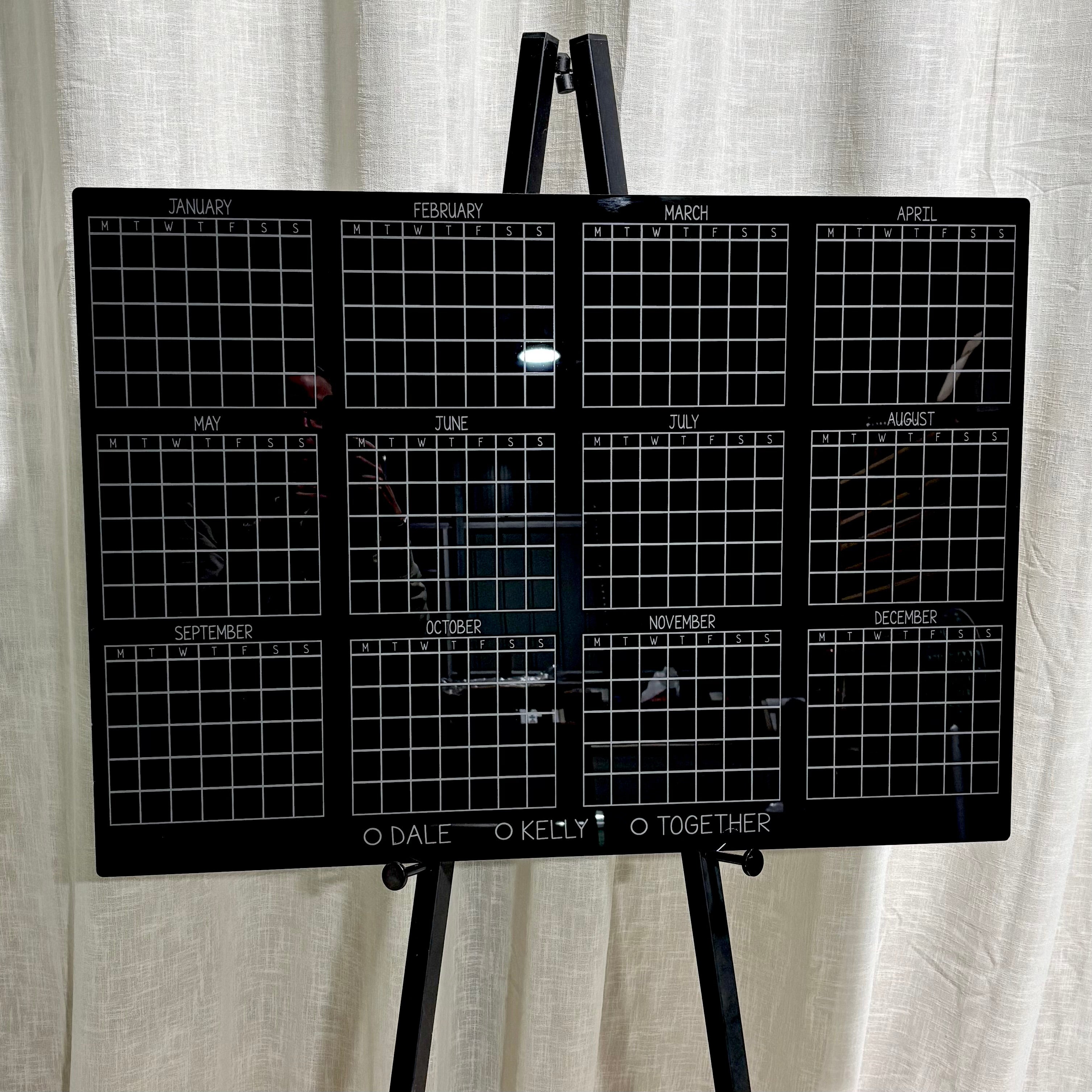 Reusable acrylic wall planner calendar, black yearly planner board with white grid, custom family organiser calendar Australia, dry erase acrylic planner for home or office, personalised yearly calendar with names, large acrylic planning board on easel, modern minimal scheduling board for couples or families