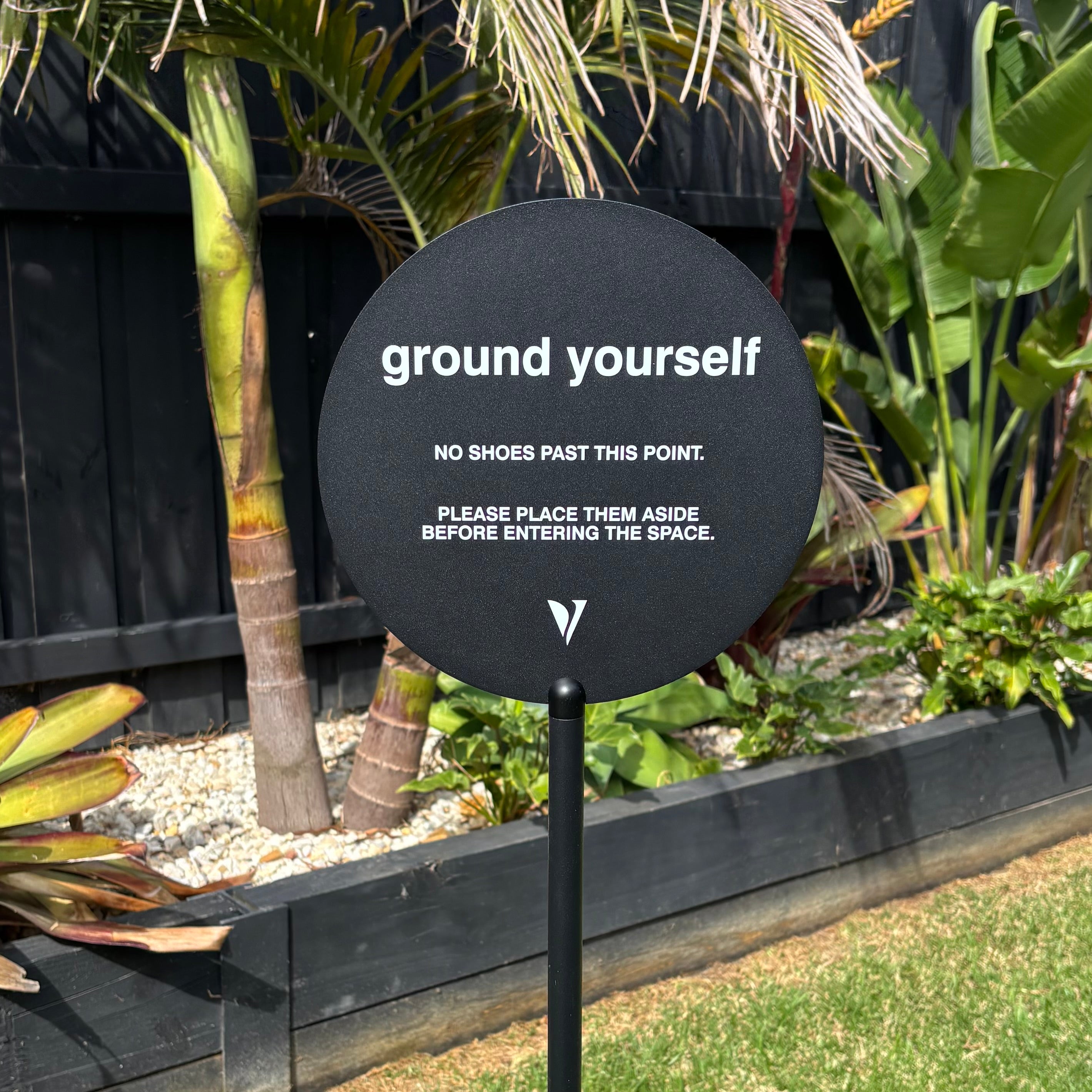 Black round freestanding sign with stand, “ground yourself no shoes past this point” custom business signage, outdoor acrylic round sign for wellness studio or spa, modern minimal entry sign Australia, yoga studio signage with stand, matte black hospitality or clinic display sign for barefoot policy