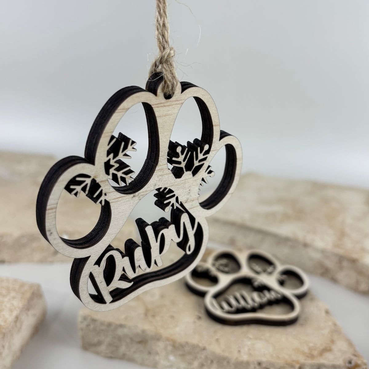Personalised laser cut wooden paw print Christmas ornament featuring the name Ruby, decorative snowflakes and natural twine for hanging on a Christmas tree.