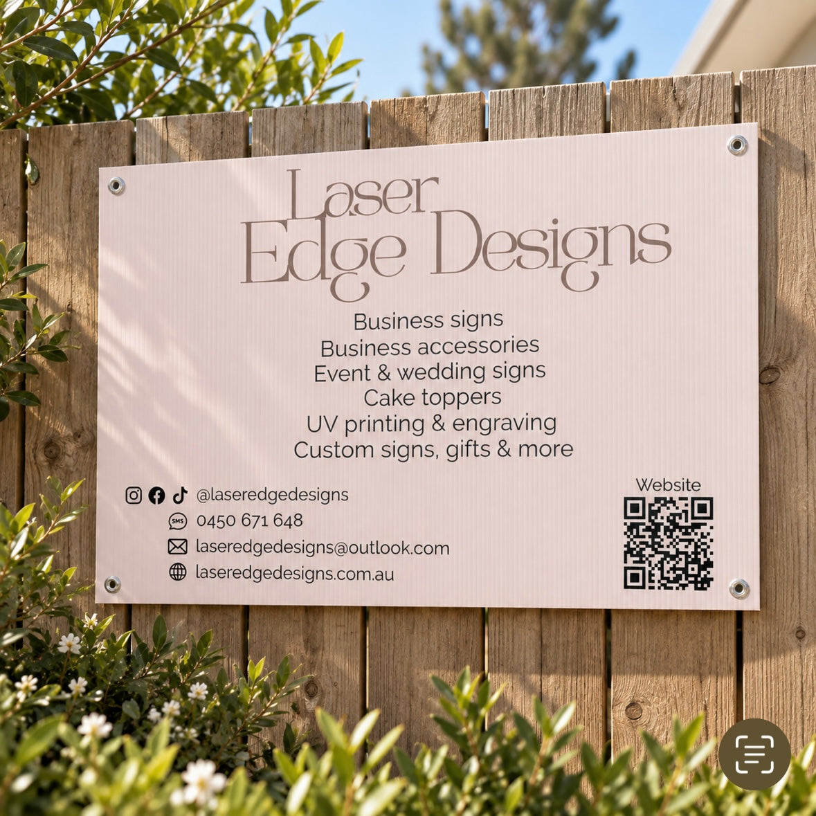Custom outdoor corflute business sign for Laser Edge Designs with printed services, contact details and QR code, mounted on a wooden fence.