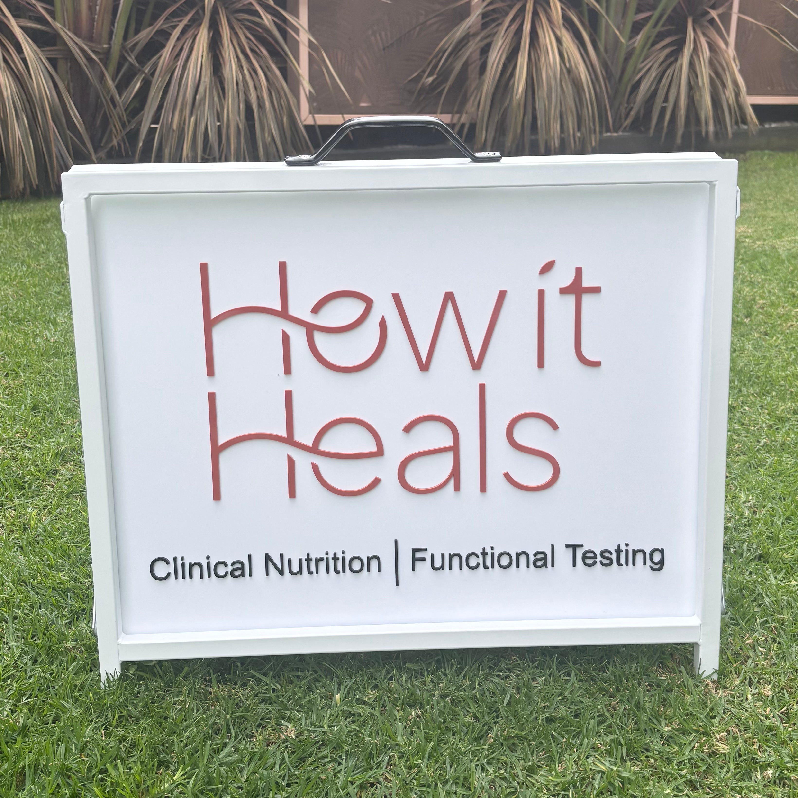Custom white A-frame business sign with 3D acrylic logo and lettering for How It Heals, featuring clinical nutrition and functional testing branding.