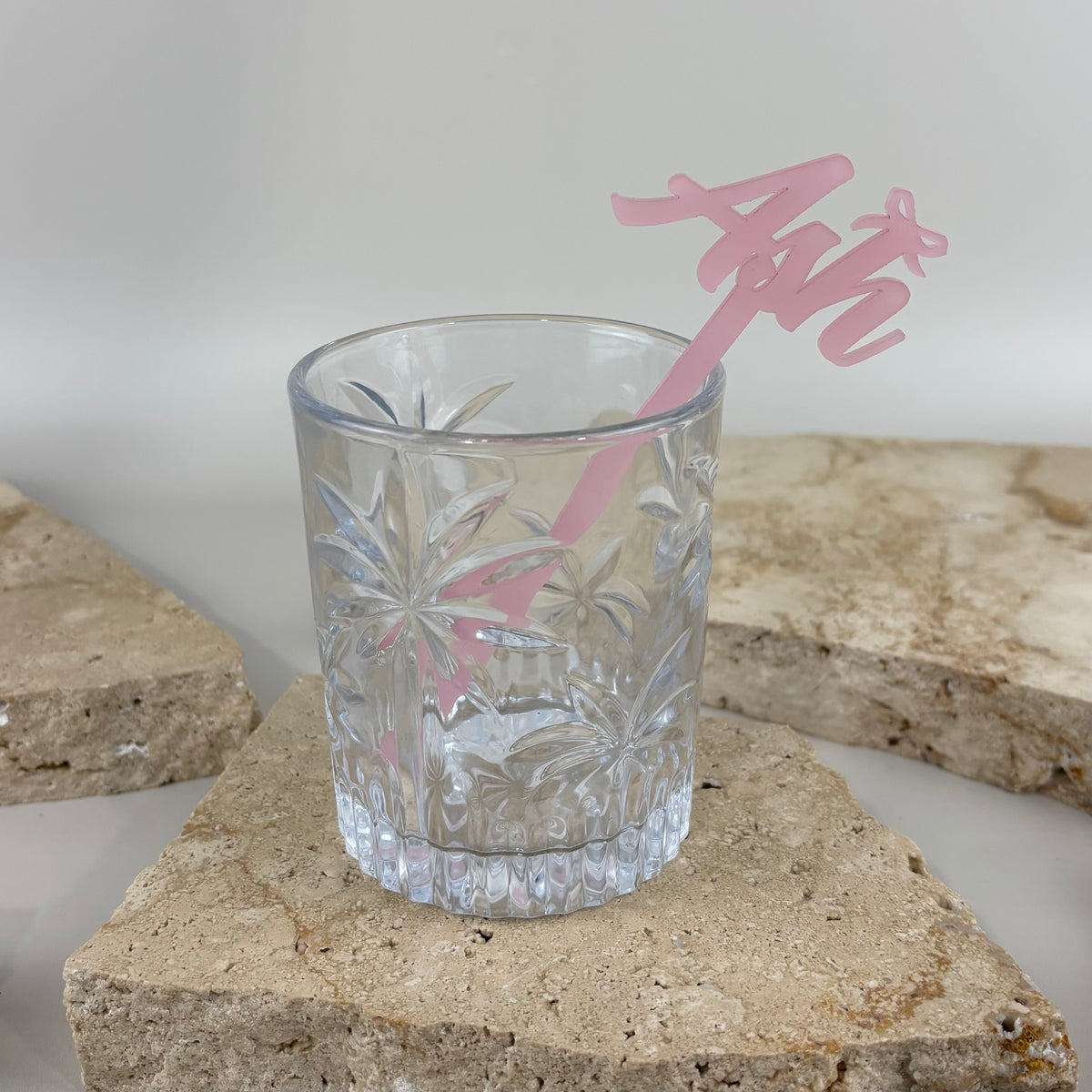 Pink personalised acrylic drink stirrer with script name, styled in a clear cocktail glass.