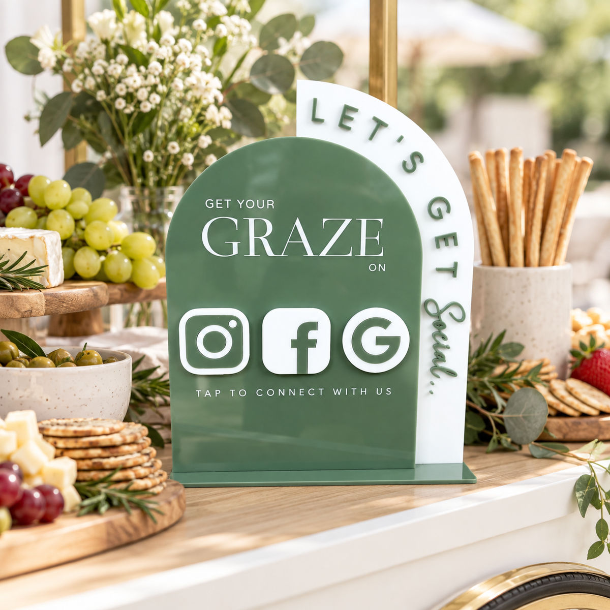Custom acrylic NFC social media stand with Instagram, Facebook and Google tap-to-connect icons, displayed on a grazing cart with cheese, crackers and fruit.