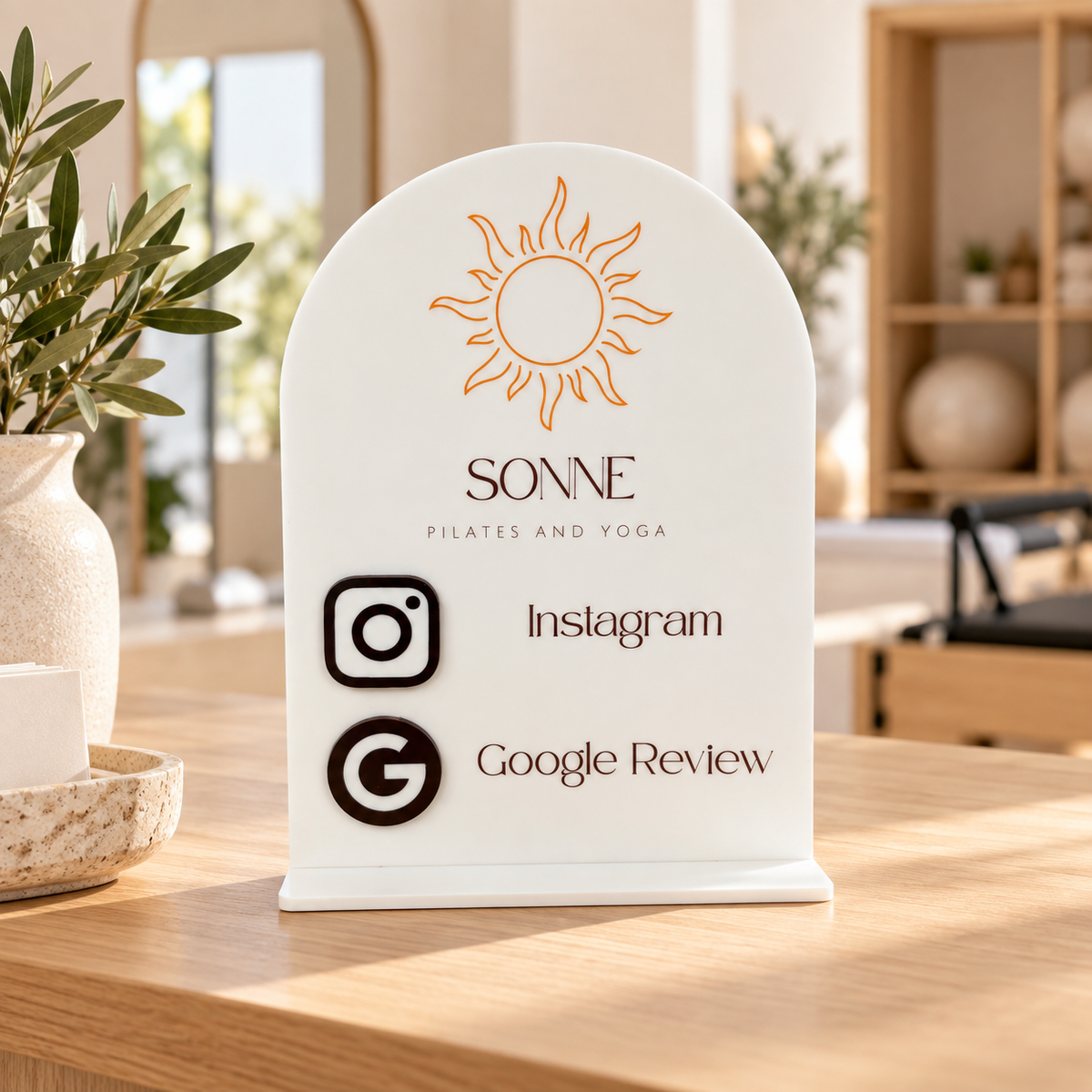 Custom NFC Instagram and Google Review stand for a Pilates and yoga studio, displayed on a timber reception counter with raised 3D acrylic icons and branding.