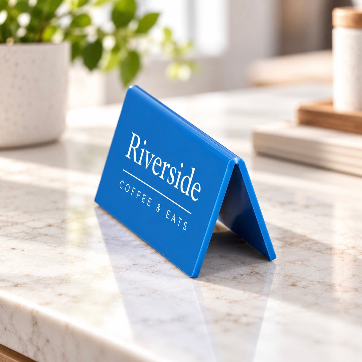 Custom blue acrylic A-frame counter sign with white business branding, displayed on a modern café countertop.