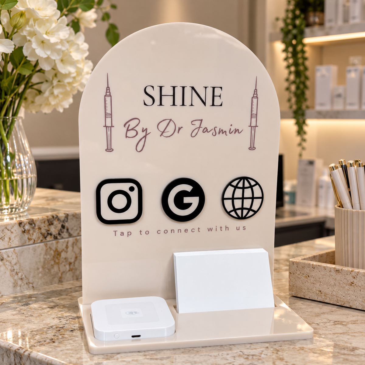 Custom acrylic NFC business station for an aesthetic clinic, featuring Instagram, Google and website tap-to-connect icons, Square Reader and business card holder on a clinic reception counter.