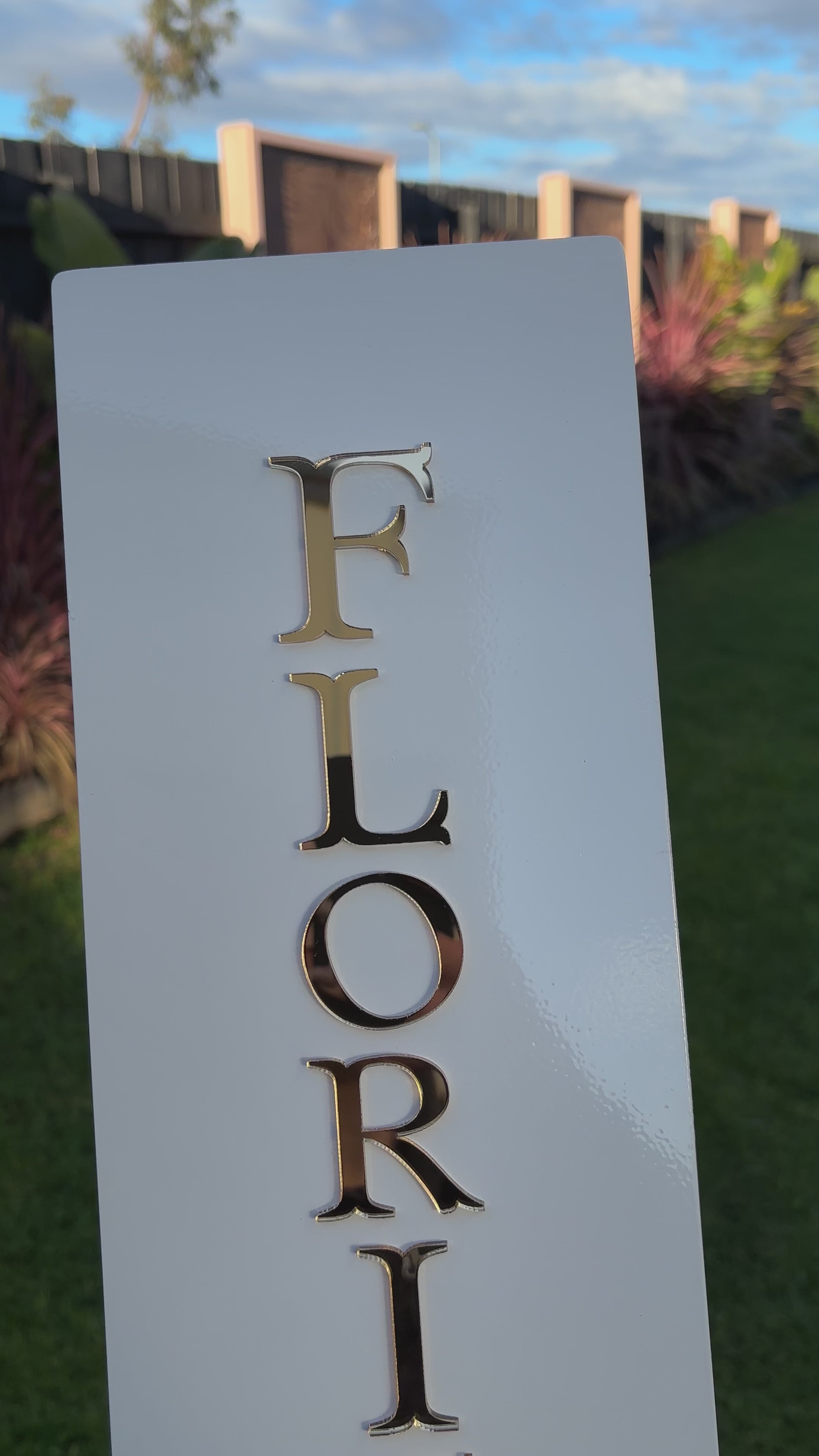 Close‑up of custom vertical blade sign with gold raised letters spelling ‘FLORIST’, shown in outdoor setting. Video 