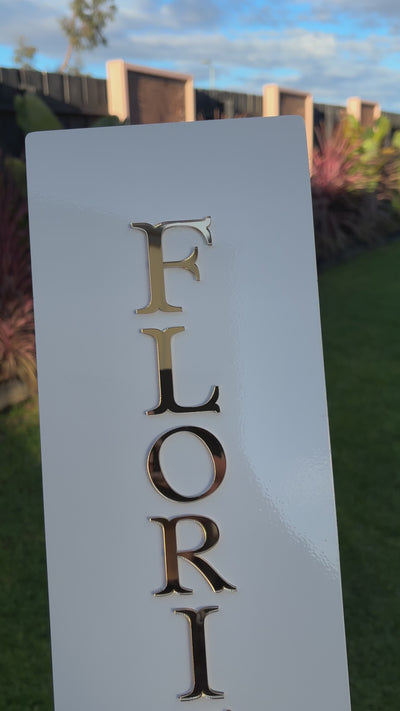 Close‑up of custom vertical blade sign with gold raised letters spelling ‘FLORIST’, shown in outdoor setting. Video 