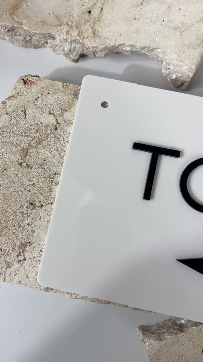 Close-up video of white acrylic toilet direction sign featuring 3D black text and arrow, showing size, gloss finish, and professional signage quality by Laser Edge Designs Australia.