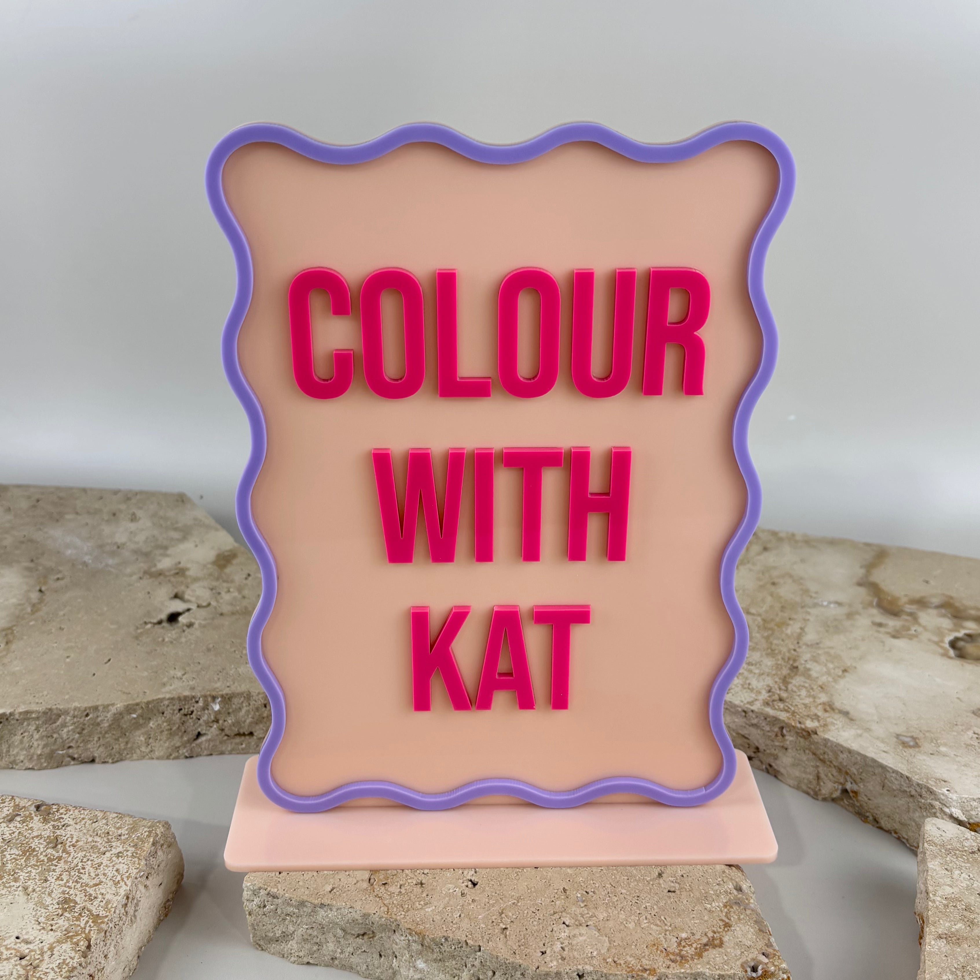 Custom colourful acrylic countertop sign with wavy purple border and raised pink 3D lettering reading “Colour With 