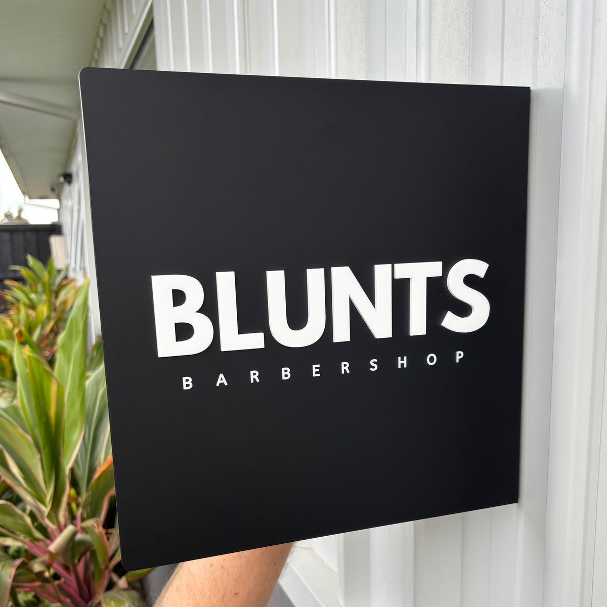 Custom black acrylic business sign with raised white 3D lettering for Blunts Barbershop, mounted on an exterior wall.